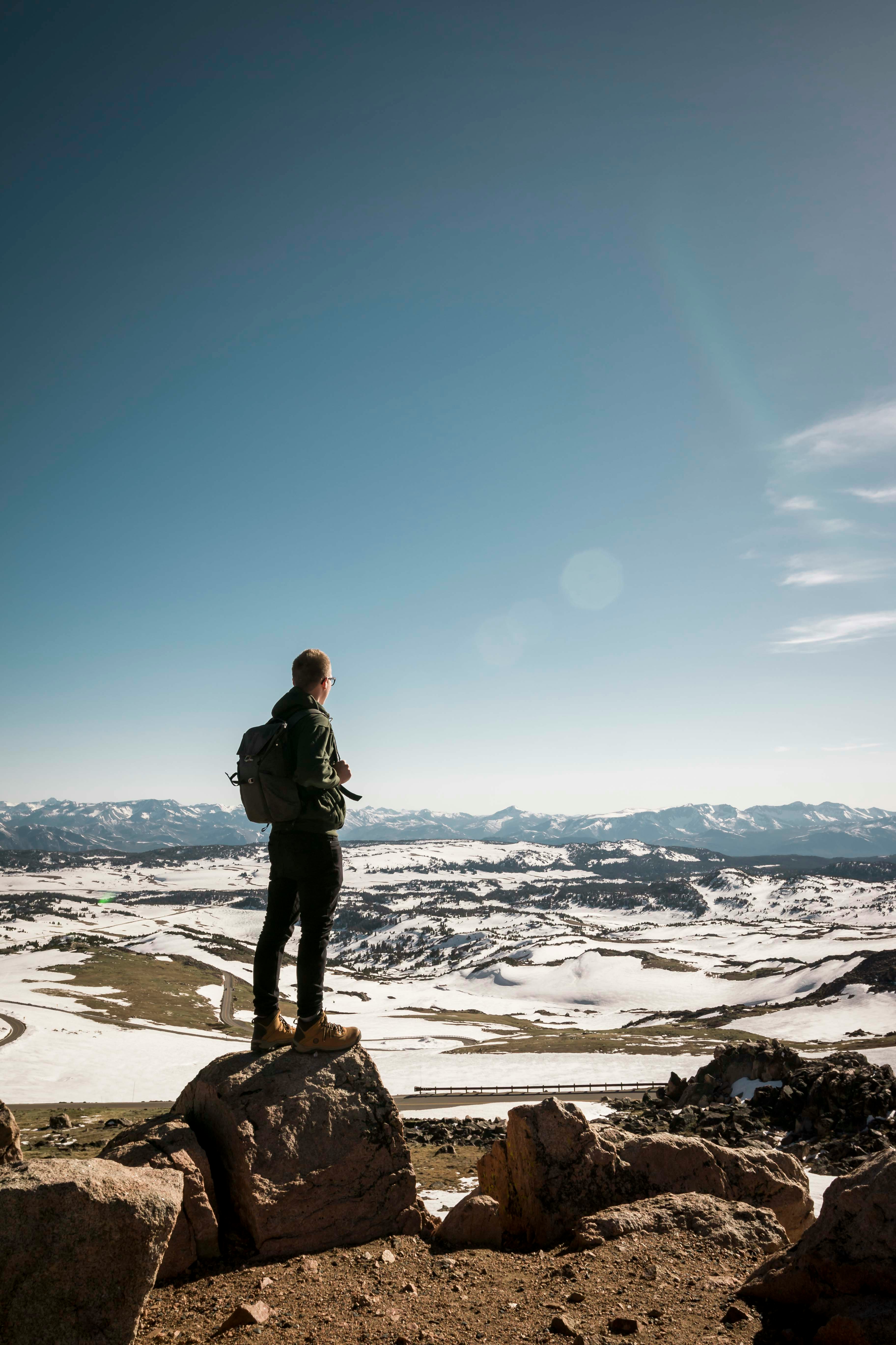 man standing on stone overlooking snow-capped mountain